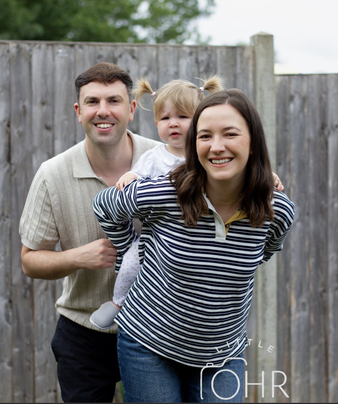 Mum and dad in the garden holding their little girl between them