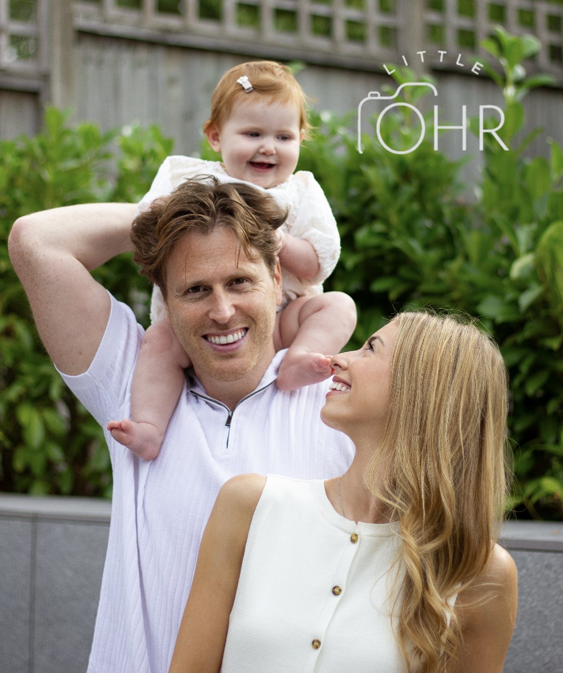 Baby on dad's shoulders while mum looks up laughing in the garden