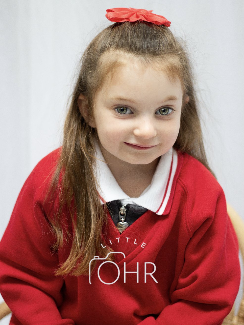 Girl with a red flower bow leaning forward in her red school jumper
