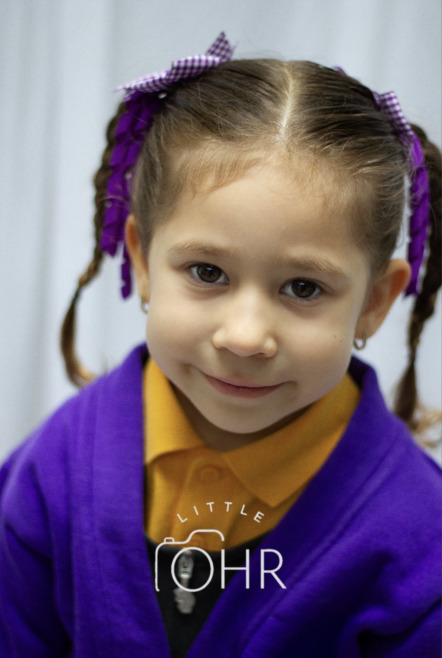 Girl with purple gingham bows in her plaits and a purple cardigan