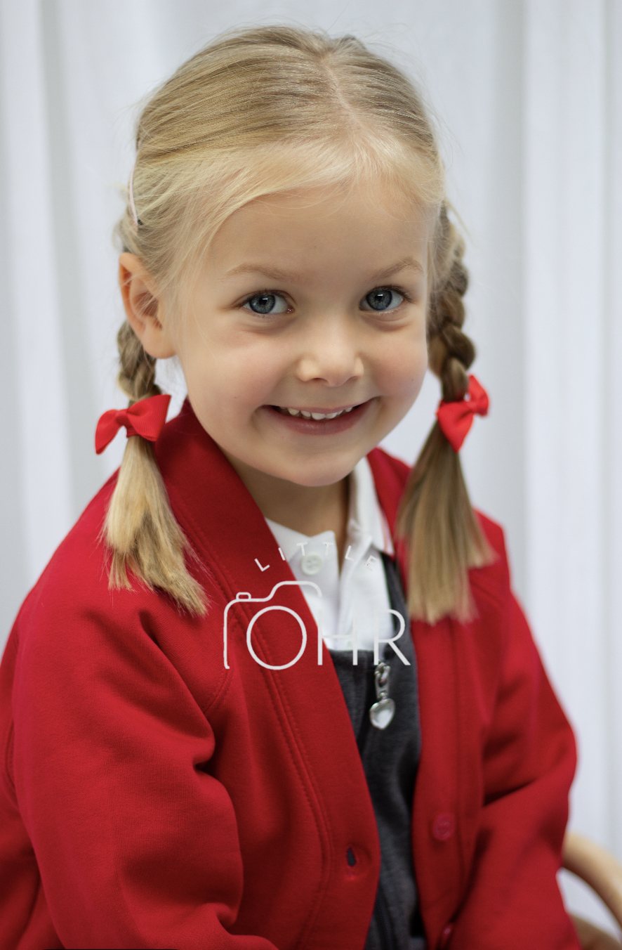 Smiling girl with plaits and red bows in a red school cardigan