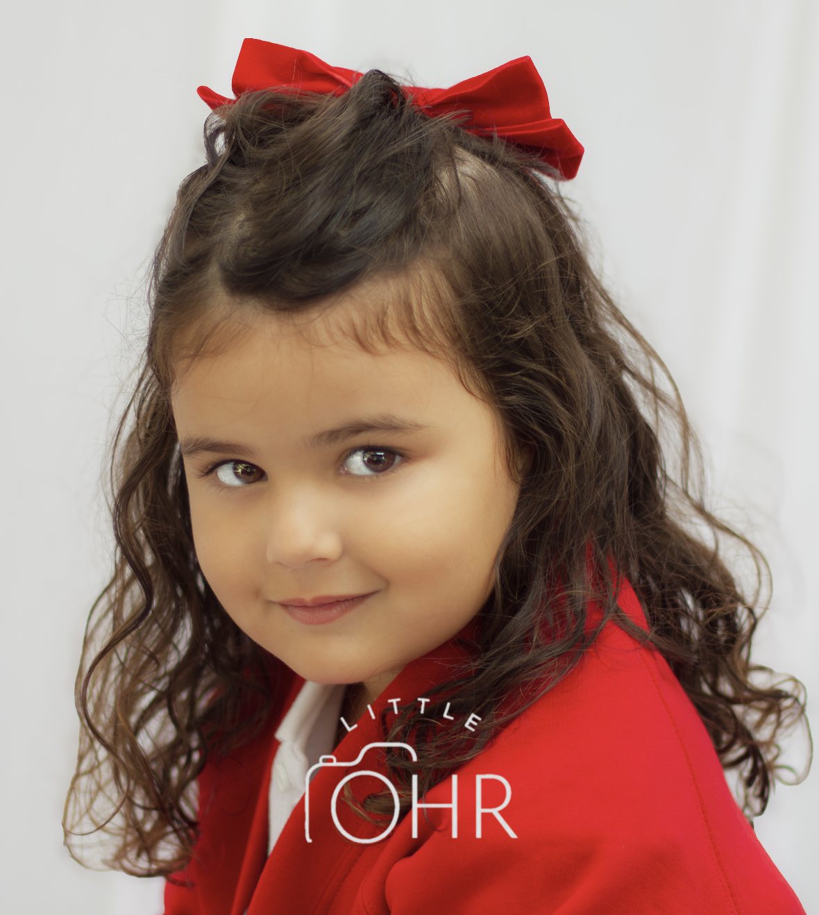 Girl with a red velvet bow and dark curls glancing over her shoulder