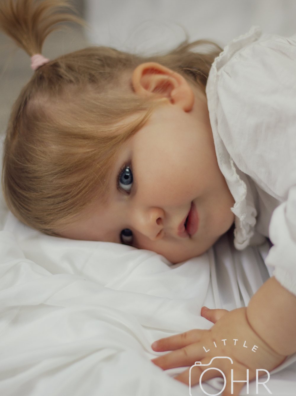 Baby girl lying on soft white bedding looking up at the camera